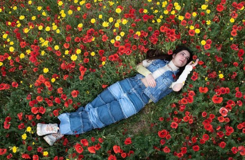 Young happy girl resting in the field of red poppy flowers. Drone aerial of woman in spring