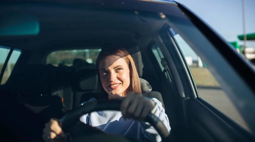 Woman smiling while confidently driving a car in daylight