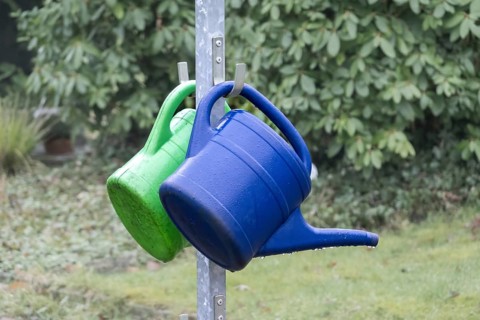Blue and green watering cans hanging on a metal stand outdoors