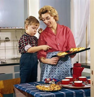 Baking in the 1950s. A mother with her son in the kitchen. She has freshly baked buns and cakes