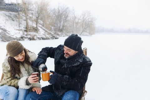 Happy lovely middle-aged couple in warm clothes drinking hot tea during romantic winter date in