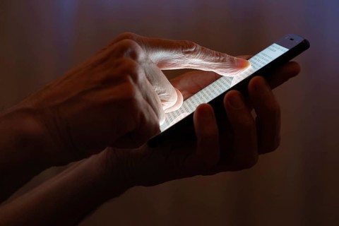 Man typing with the finger on the touch screen of a black smartphone close to the window with