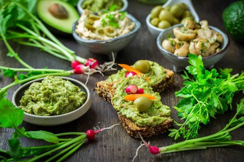 Wholemeal bread with avocado spread and vegetables on wooden kitchen table