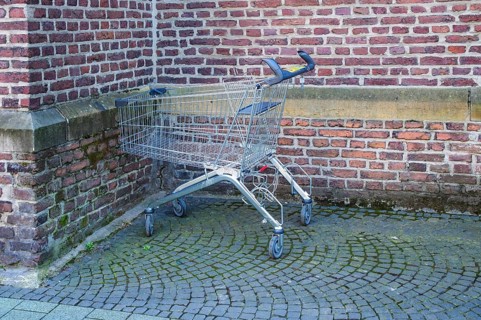 Metal shopping cart stands empty next to a brick wall on a cobblestone street, symbolizing