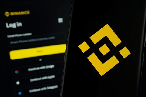 Binance logo is displayed on a smartphone screen, with the binance login page visible on a computer