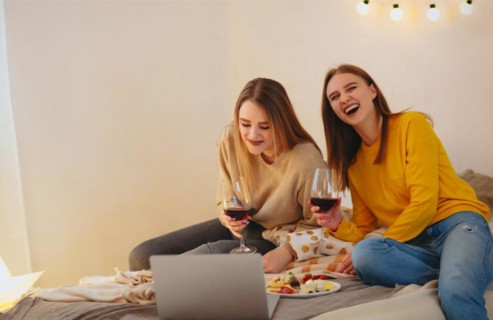 Two cute happy funny women friends having fun together, arranging home cinema evening, watching