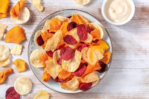 Various vegetable chips with a homemade dip, shot from the top on a rustic wooden background with a