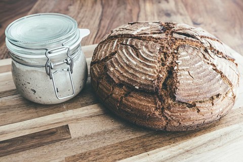 Freshly baked homemade rye sourdough bread and sourdough starter in jar on wooden table