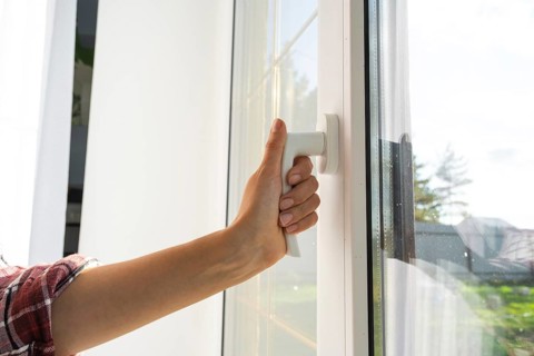 The hand holds the handle of a plastic double-glazed window, closing and opening the window with a