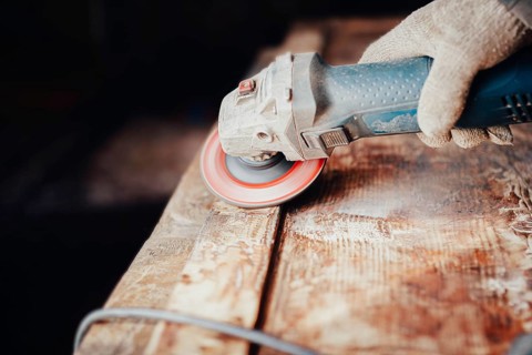 Close-up of an angle grinder being used on a wooden table by a gloved hand
