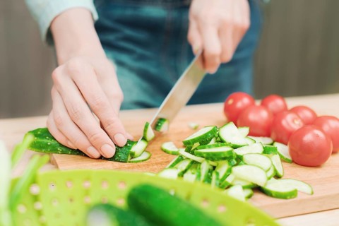 Close-up of female hands cut into fresh cut cucumbers on a wooden cutting board next to pink