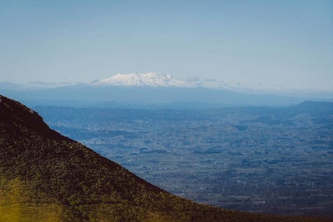 Snow-capped mountains on the horizon, hills in the foreground and blue sky, Mount Taranaki, New