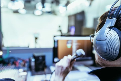 Young man is sitting in the recording studio and talks into the microphone, buttons and equipment