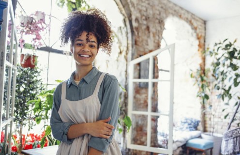 Young black woman wearing beige apron on flower shop background with copy space. Portrait of
