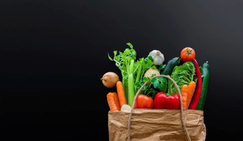 top view of fresh organic vegetables bought on weekly market in brown paper bag against dark table