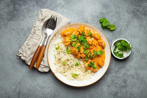 Traditional Indian dish chicken curry with basmati rice and fresh cilantro on rustic white plate on