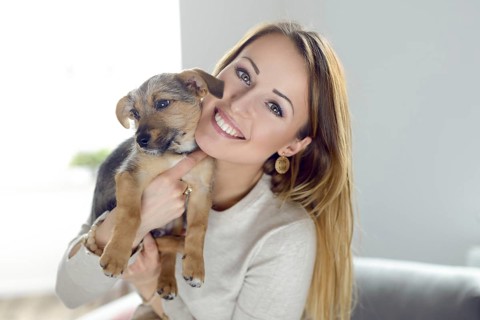 Pretty happy young woman with her pet dog held up to her cheek in her hands in a natural tender