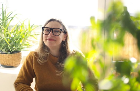 Portrait of smiling middle-aged woman wearing glasses sitting in room with green potted