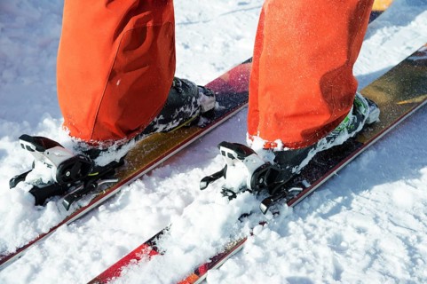 Orange alpine ski boots in a ski mount. One boot is completely fixed on skis, the second is not.