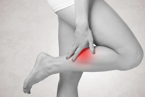 Female with pain in her lower leg, isolated in grey