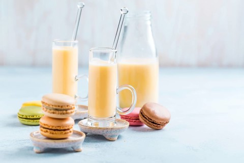 Assorted delicious French macarons with egg liqueur or eggnog on blue background
