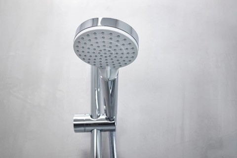 Shower head on a gray microcement wall of a modern bathroom