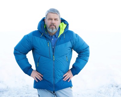 Man, 56 years old with grey hair and a full grey beard standing in front of a snowy area in winter,
