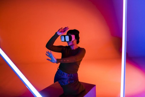 Happy female in VR headset smiling and exploring virtual reality under red neon illumination in
