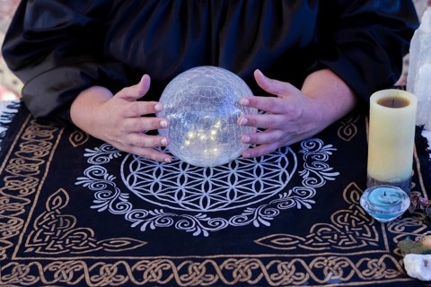 Close up of a woman fortune teller dressed in black reads the future in a crystal ball