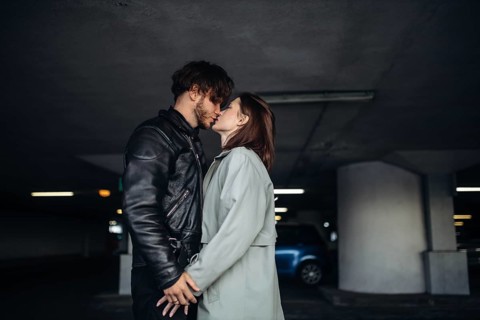 The couple shares a kiss in a dimly lit parking garage, showing intimacy and connection