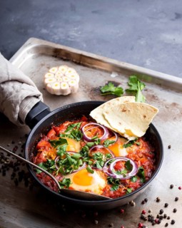 Shakshuka with pita bread in a pan. Middle eastern traditional dish. Fried eggs with tomatoes, bell