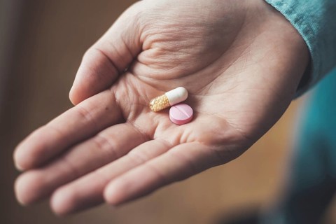 Male hand holding drug or vitamin pill in