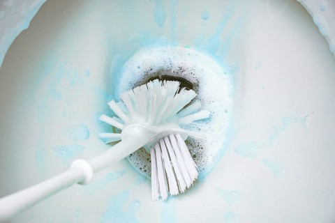 Cleaning a toilet bowl with a brush and strong chemical cleaning foam that pollutes the