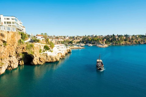 Tourist boat approaches the entrance to sea cave seen from Yavuz Ozcan Park with harbor in