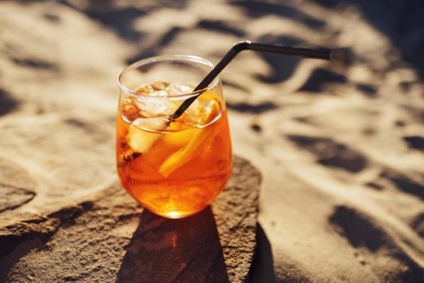 Orange slice and aperol spritz cocktail on a stone against the backdrop of a sandy beach. Glass