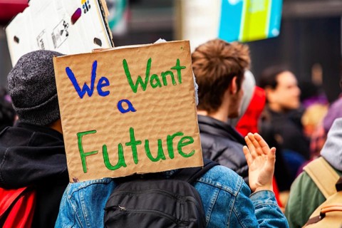 A cardboard sign is viewed close-up saying we want a future as a crowd of environmental campaigners