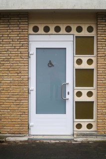 Public restroom door with accessibility sign for disabled people featuring frosted glass and white