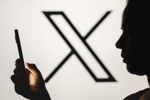 In this photo illustration, a woman's silhouette holds a smartphone with the Twitter (X) new logo