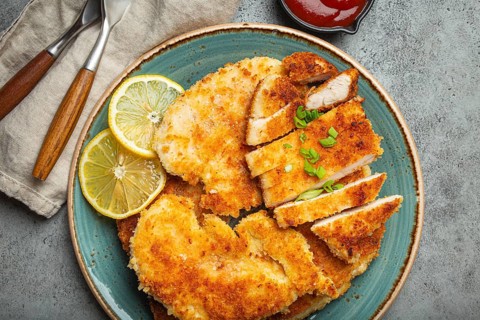 Crispy panko breaded fried chicken fillet with green salad and lemon cut on plate on gray rustic