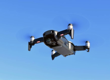 Black unmanned aerial vehicle with a camera against the blue sky