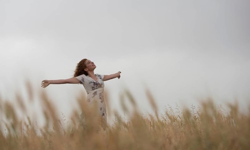 Happy woman in a floral dress stands amidst golden wheat, enjoying the serene landscape
