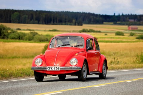 Red Volkswagen Beetle, officially Volkswagen Type 1, driving along country road on Maisemaruise