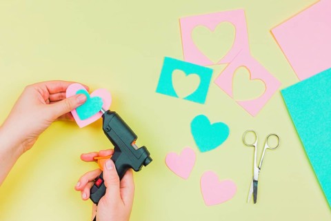 Close up woman s hand sticking paper heart shape with electric hot glue gun