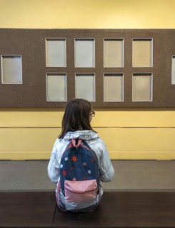 Back view of teen girl with backpack in museum visiting exhibition, schoolgirl sitting on bench in