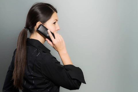 Secretive businesswoman talking on her mobile phone standing facing away from view while glancing