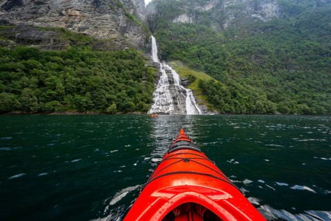 Kayak trip on the Geirangerfjord at the Freier waterfall, tip of a red kayak in the fjord,