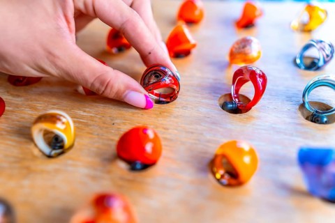 Woman's hand with pink nail polish picking up a colorful resin ring from a wooden display at a