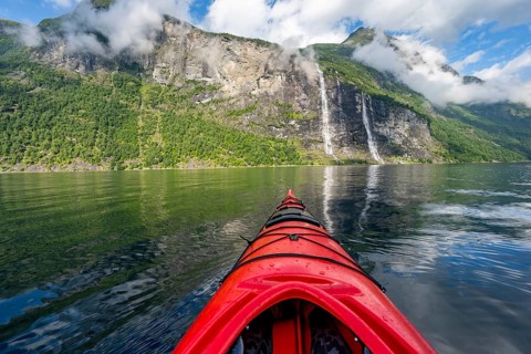 Kayak trip on the Geirangerfjord with waterfall The Seven Sisters, tip of a red kayak in the fjord,