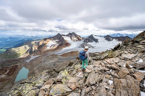 Mountaineer with helmet on a rocky hiking trail, in high mountain landscape, view of blue glacial