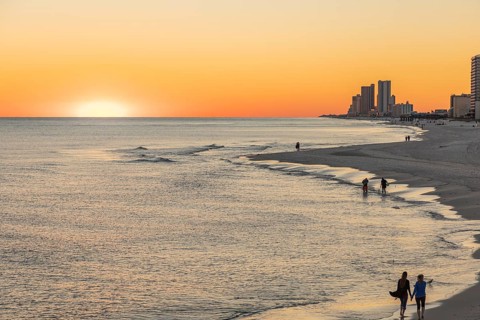 People walking and playing on the beach as the sun sets over the Gulf of Mexico at Gulf Shores,
